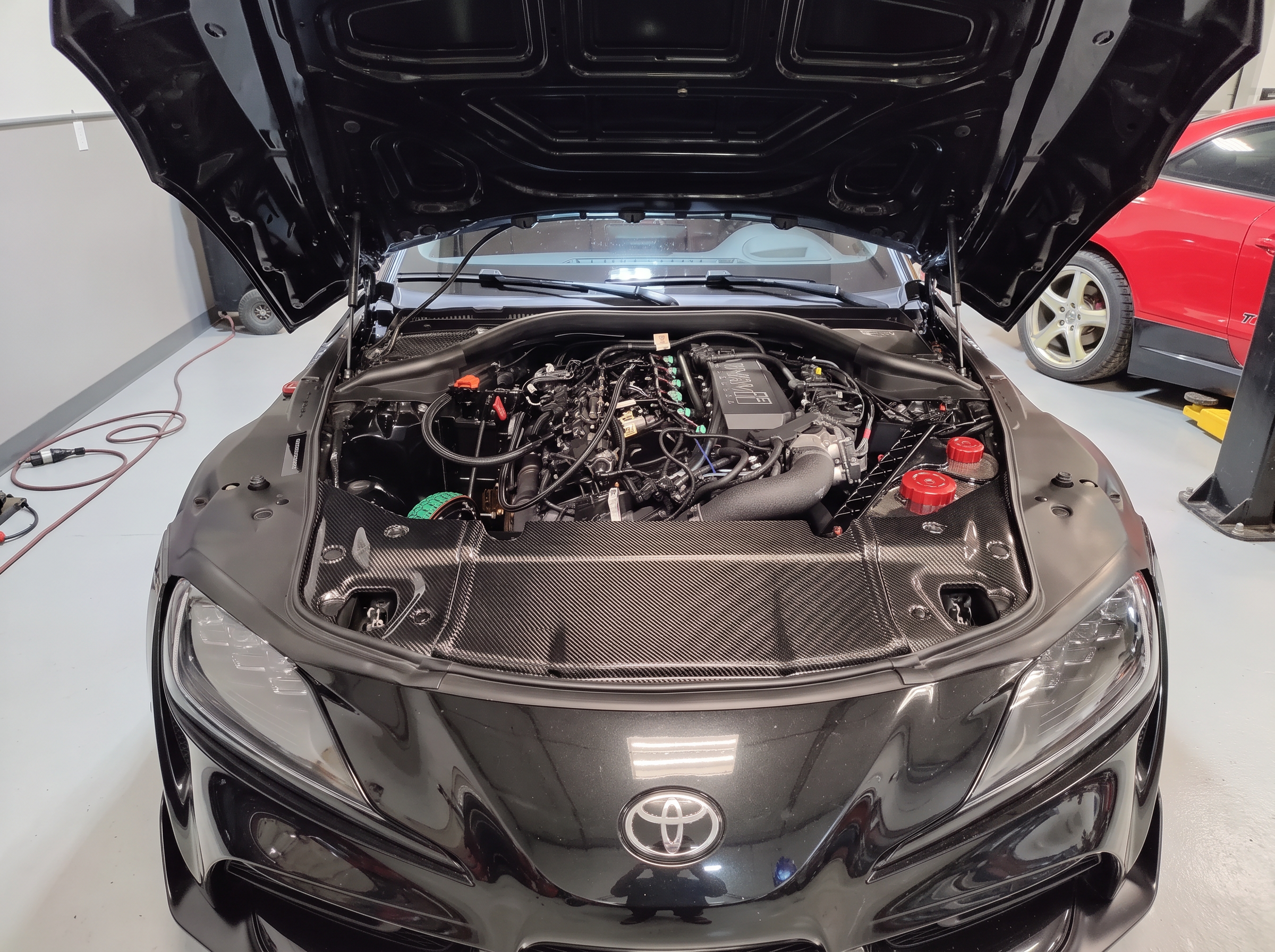 Toyota GR Supra with hood up showing the engine and carbon fiber cover